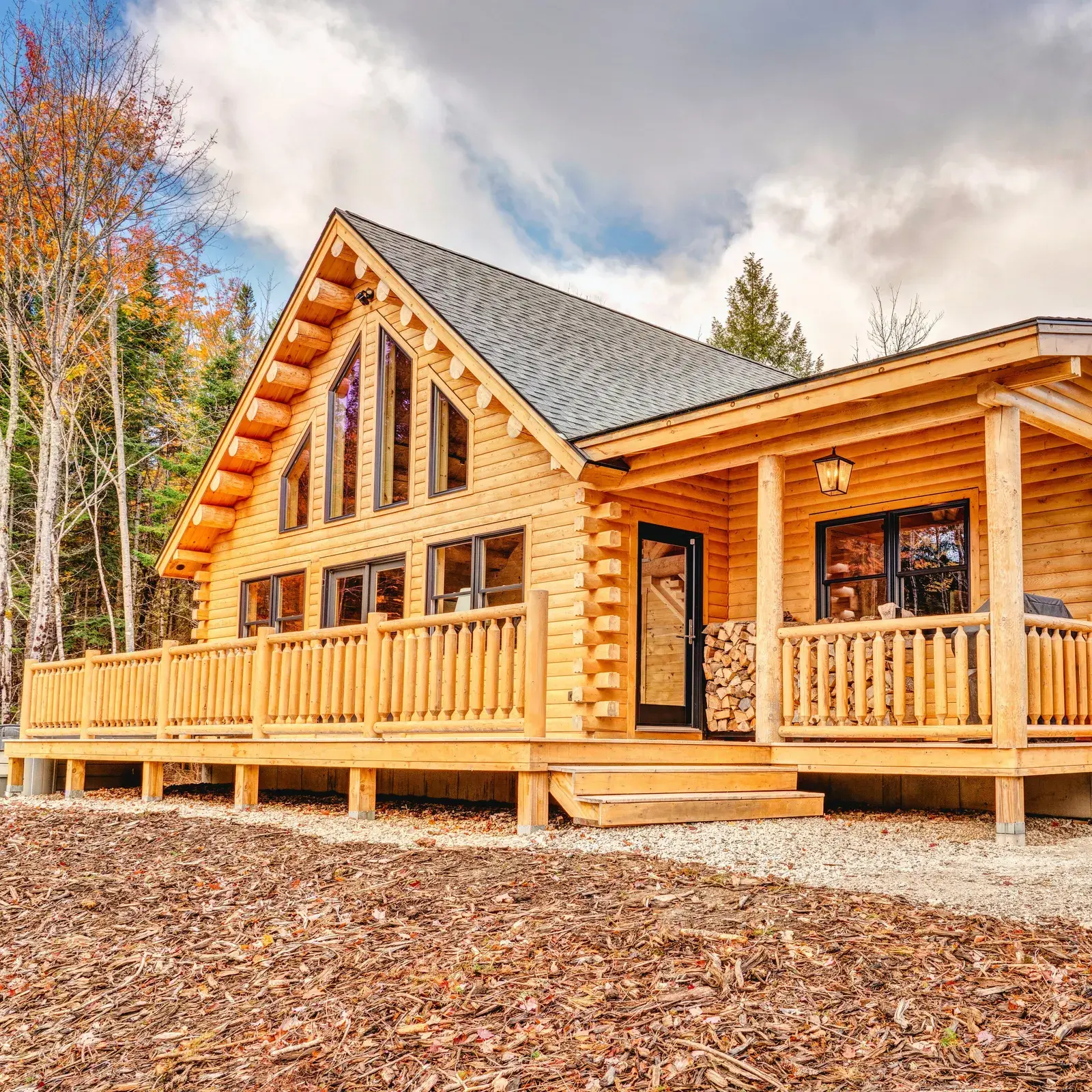 Cedar log home with a covered porch, stacked corners, and tall gable windows at the edge of the woods