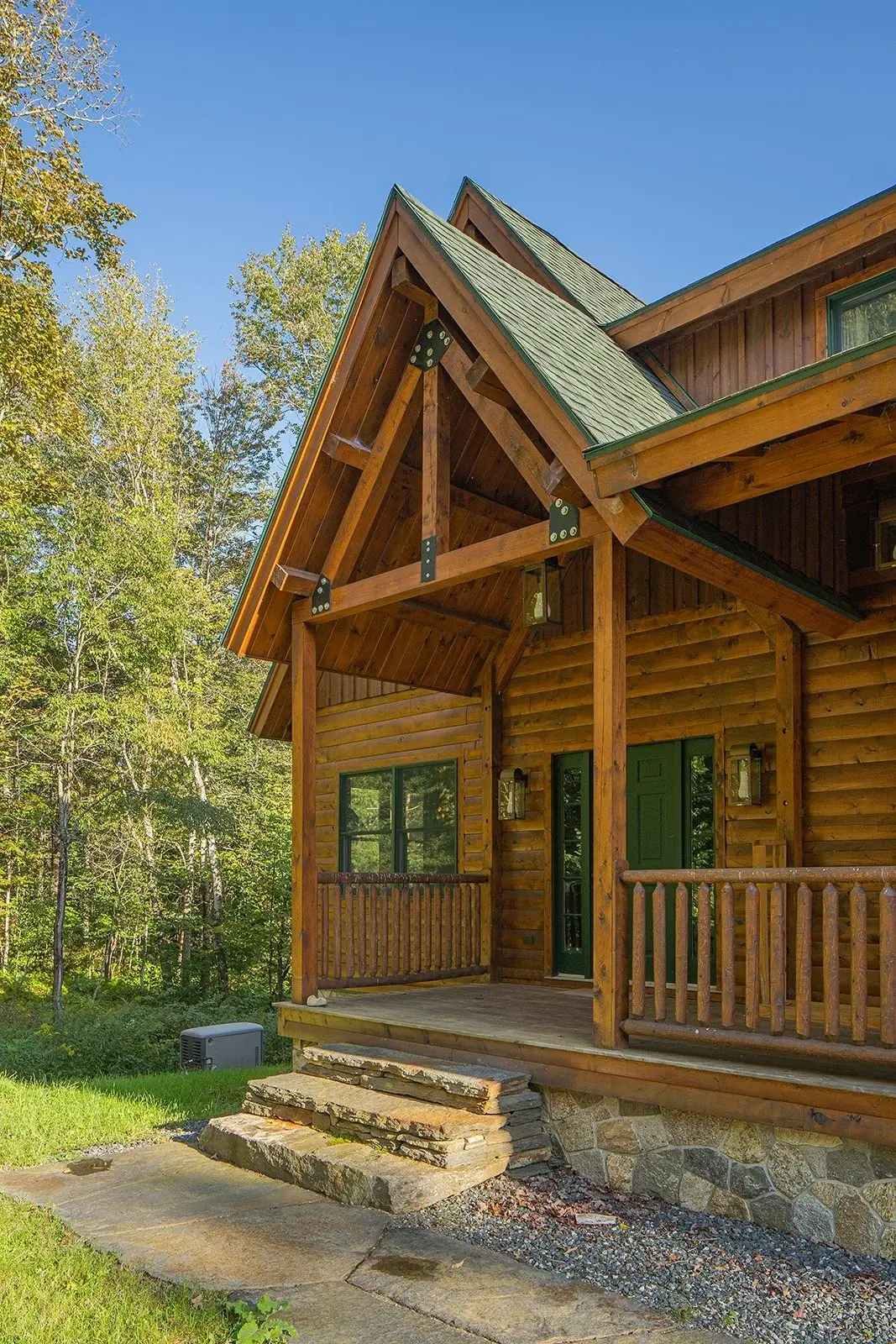 The covered front porch feels especially sturdy with stone steps, dark stained cedar, and rugged black truss plates. The wide front door is well-lit with both wall mounted and pendant lanterns, creating a welcoming entrance. 
