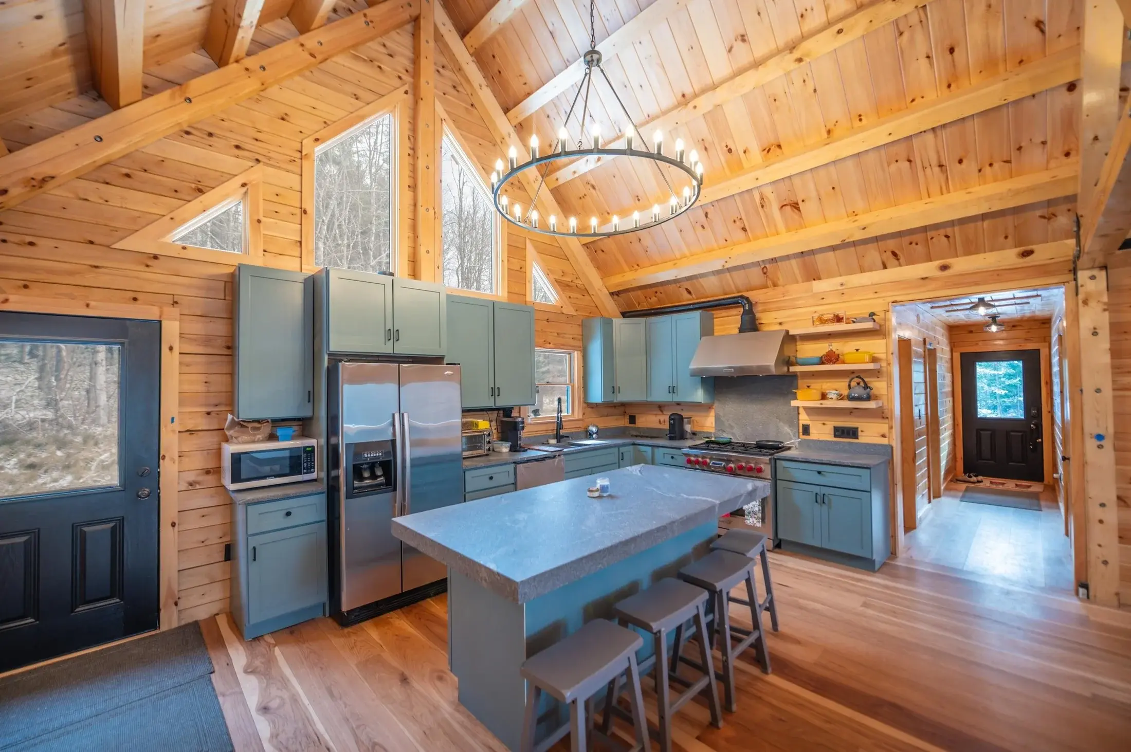 Muted turquoise cabinets add a cheerful pop of color, complementing the natural wood of the ceilings, walls, and floors. Slate gray soapstone countertops and understated bar stools add a soft, organic feel to the kitchen, while black hardware and fix