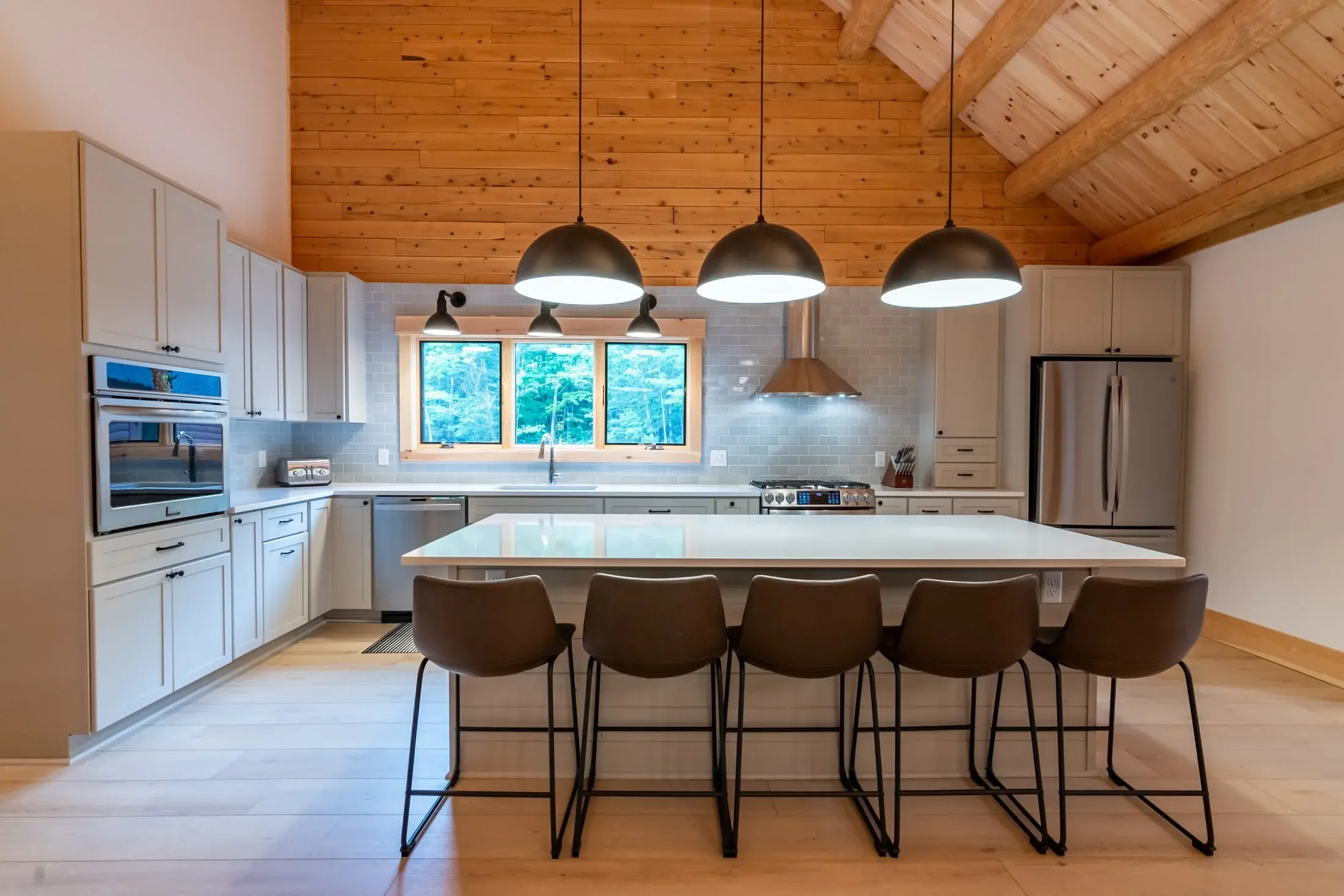 The modern look of this kitchen feels just right under the rustic cedar log ceiling. The secret to blending these two seemingly opposite styles is quite simple- by keeping the cabinet and chair colors neutral and incorporating natural stone on the ba