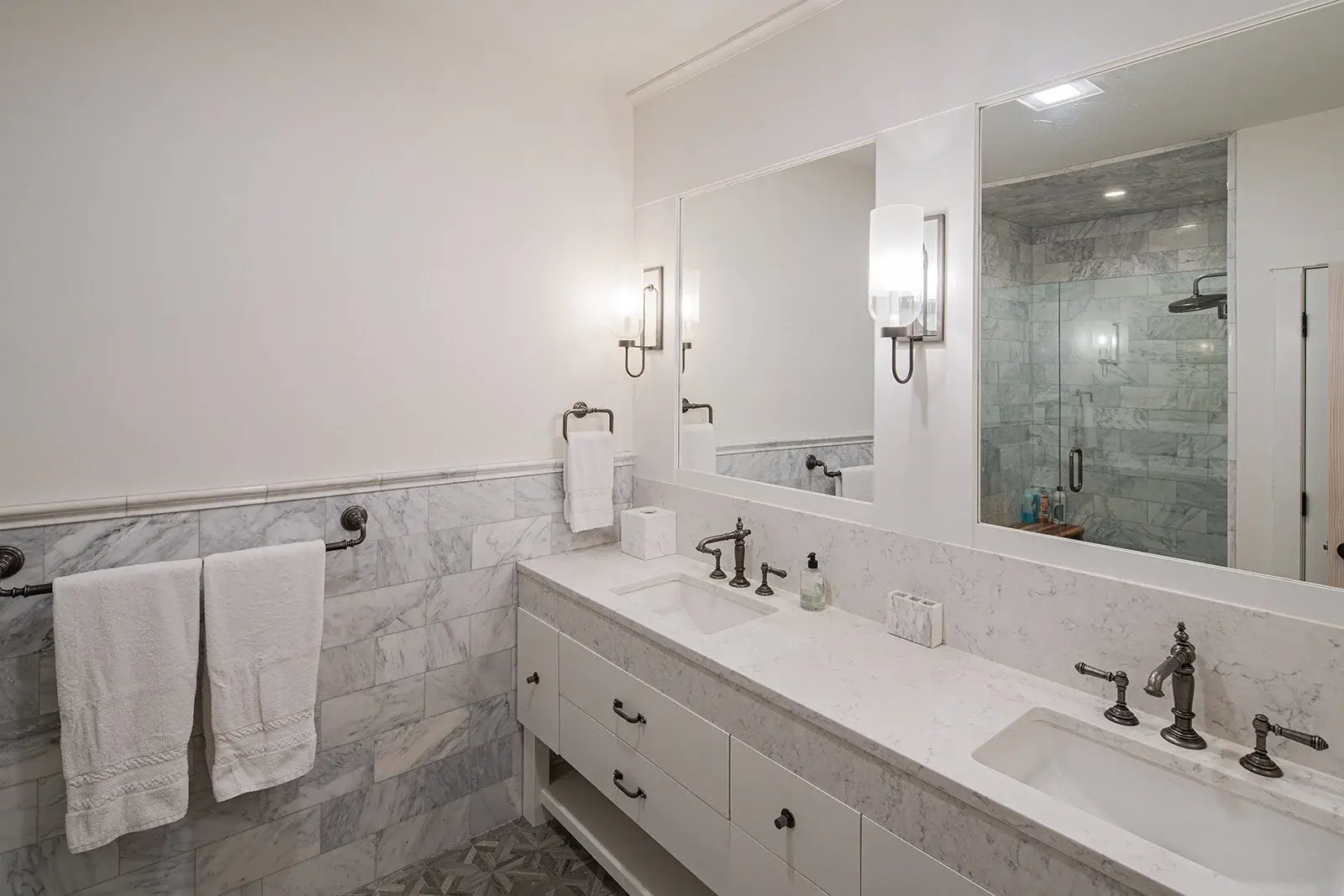 Crisp white walls and a soothing collection of gray and white marble combine to create a refreshing spa-like bathroom. A bright contrast against the warm, rustic feel of the main living areas, the design utilizes a simple color palette and classic ha