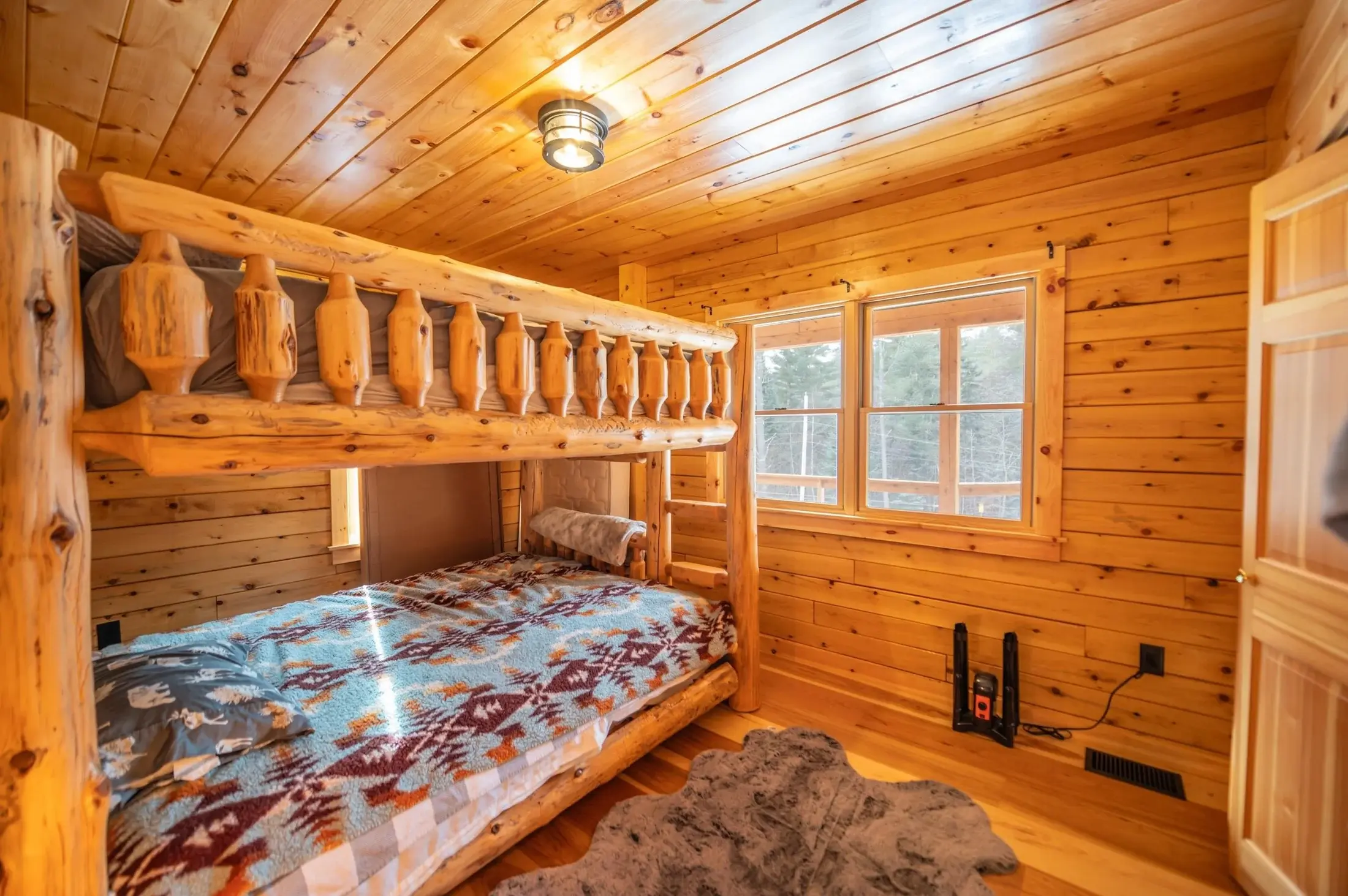 The main floor bunk room is a cozy retreat, with a sturdy log bunk bed, colorful bedding, and a big soft area rug to tie it all together. 