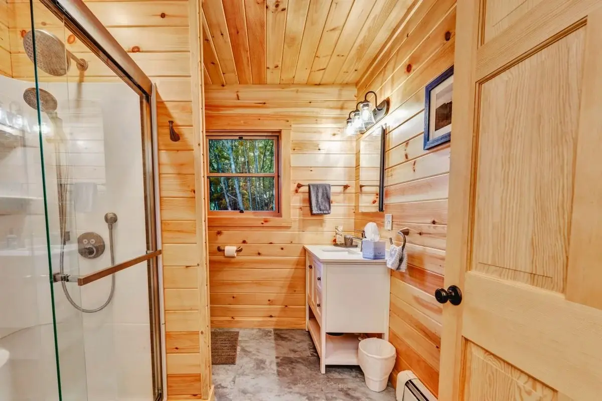 The main floor bathroom features fresh white cabinetry and a glass shower door, a clean and bright contrast to the warm wood walls and ceiling. 