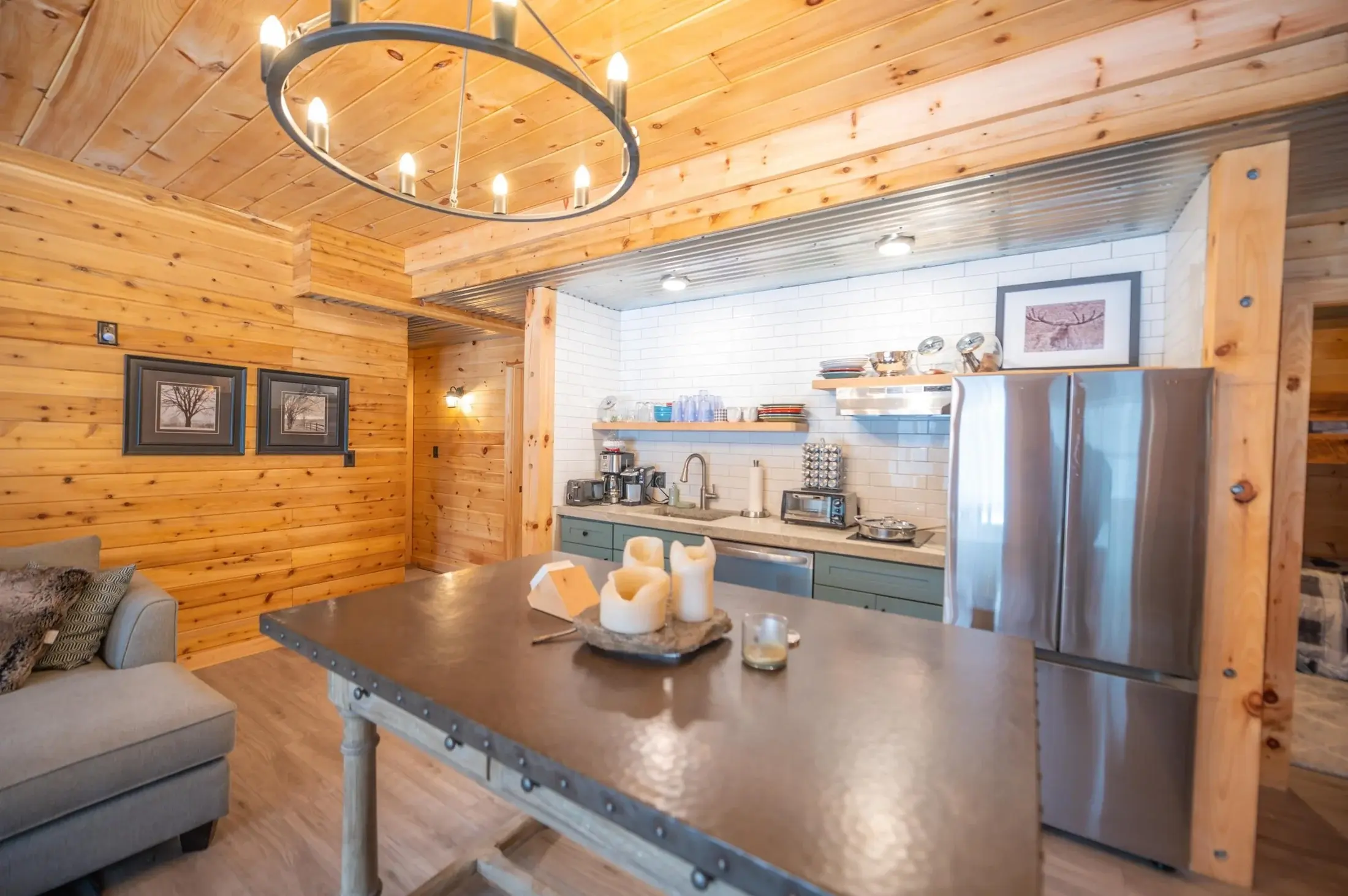 A full-sized fridge, large island, and statement lighting upgrade this kitchenette into a hardworking and beautiful space. The corrugated metal ceiling reflects additional light and creats a crisp complement to the white tiled backsplash. 
