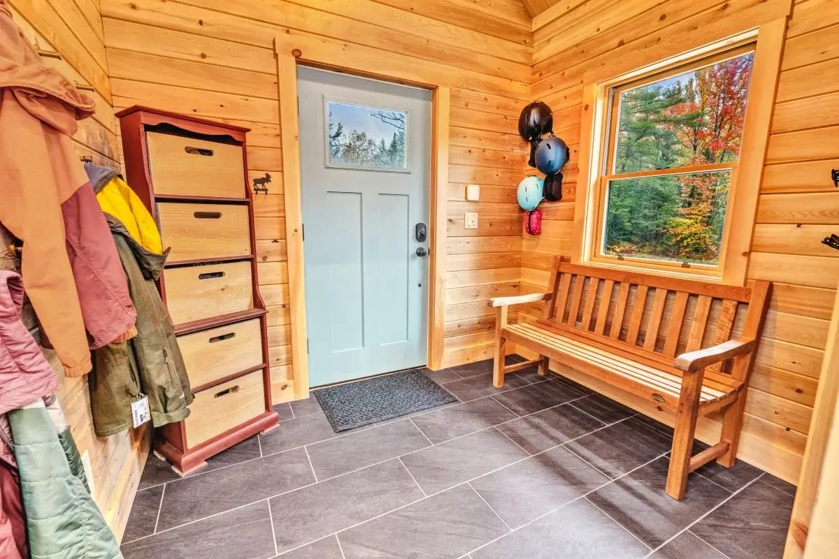 The mudroom offers a cheerful welcome, with plenty of natural light and practical storage solutions on every wall. A sturdy wooden bench, large stone tiles, and wooden walls and ceiling make for a seamless transition from outdoor adventures.   