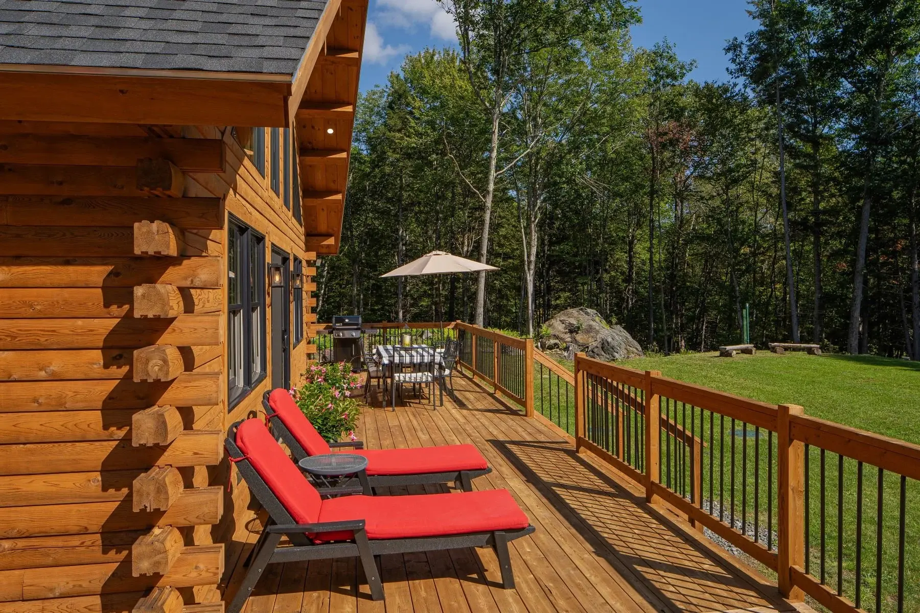 The wraparound deck offers plenty of space for outdoor dining, relaxing, and entertaining. The square railing with black metal balusters adds a modern touch to the rustic logs. 