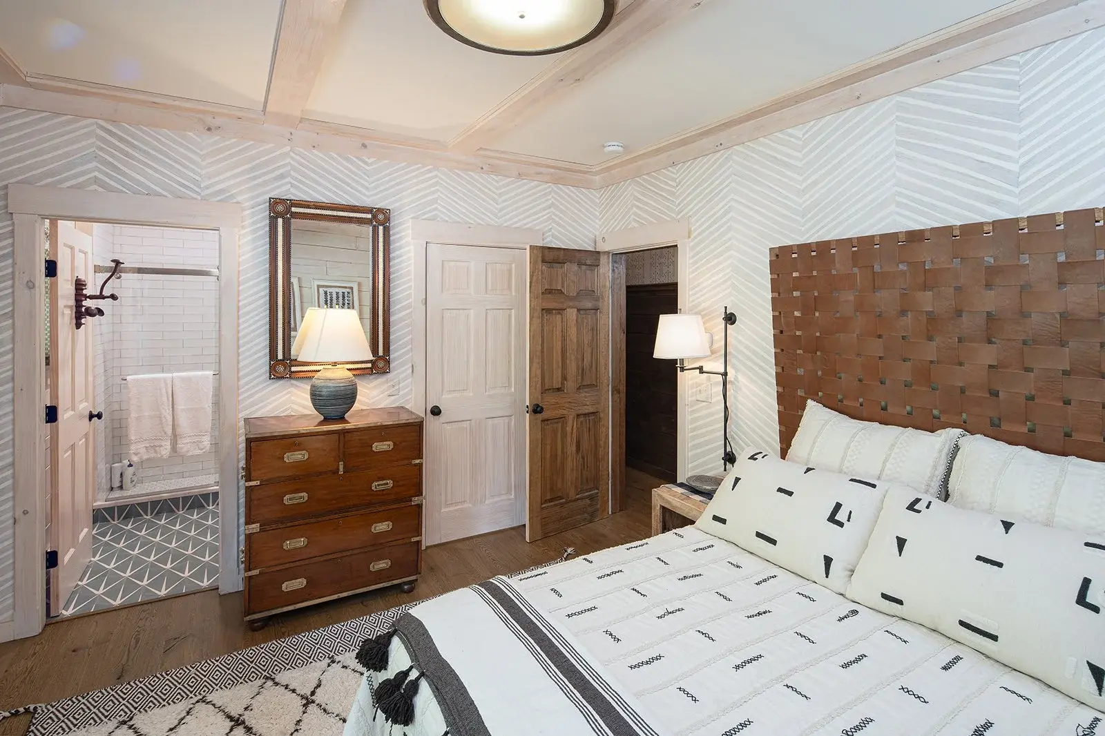 The primary bedroom is artfully designed with geometric patterns throughout, while still maintaining an organic softness by layering a variety of natural materials. Pickled white wood blends effortlessly with the creamy white and gray wallpaper, crea