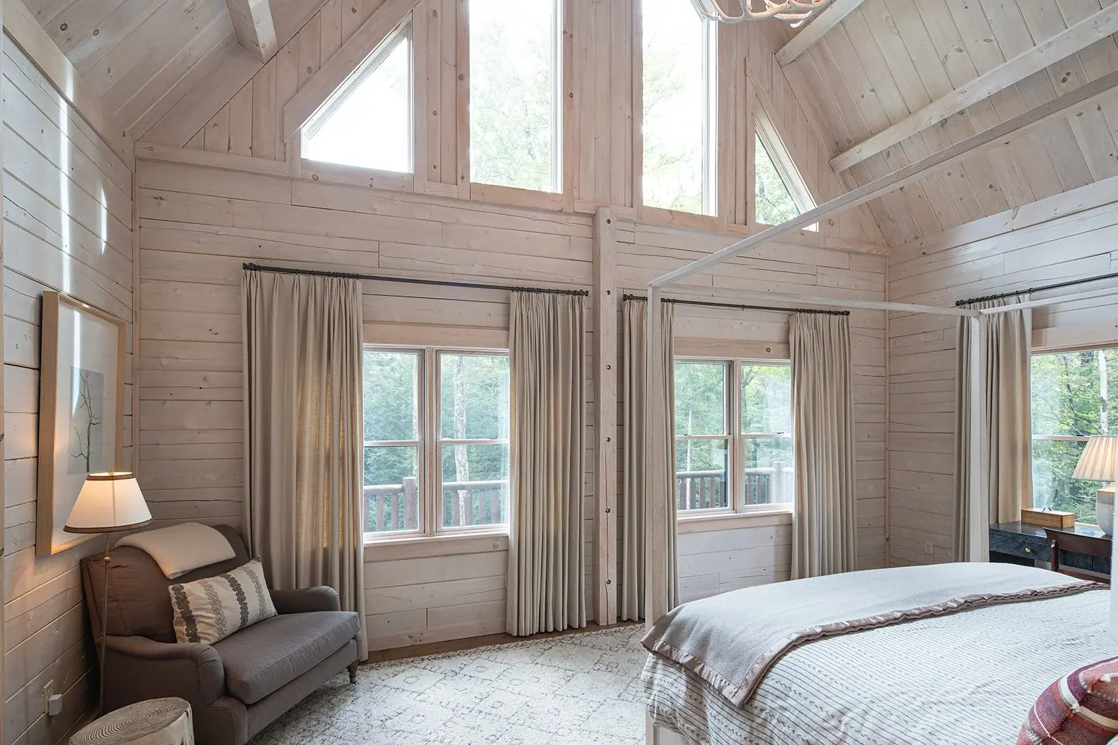 Soaring cathedral ceilings with windows to the top are a hallmark of a cedar log home, and this bedroom is an elegant example of that classic style. White pickled wood throughout creates a light and airy feel to balance the rugged exposed beams and w