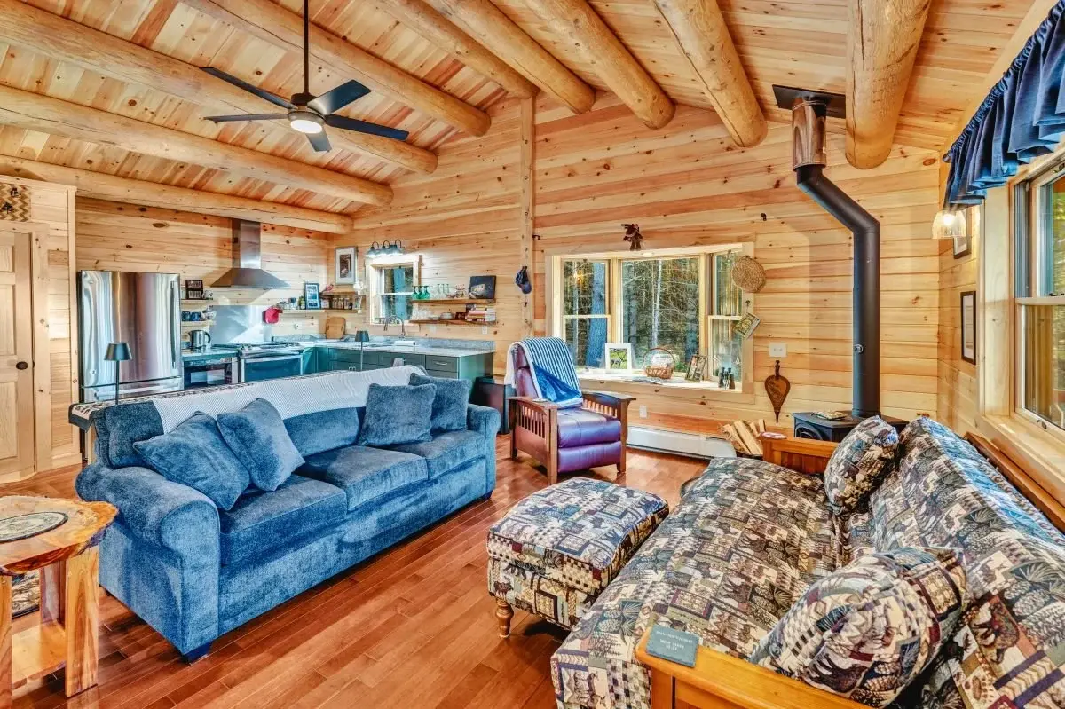 The open-concept living room showcases the natural beauty of Northern White Cedar. Full log beams frame the vaulted ceiling for a traditional log cabin look. 