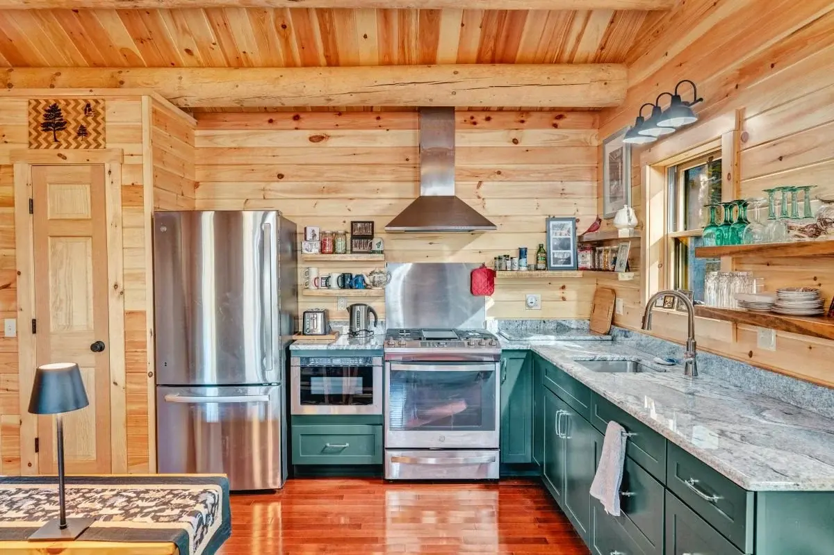 The kitchen embodies the casual elegance of log home style, blending sleek metal, rugged log, and sparkling stone, tied together with dark jade cabinets for a functional space with a lot of personality. 