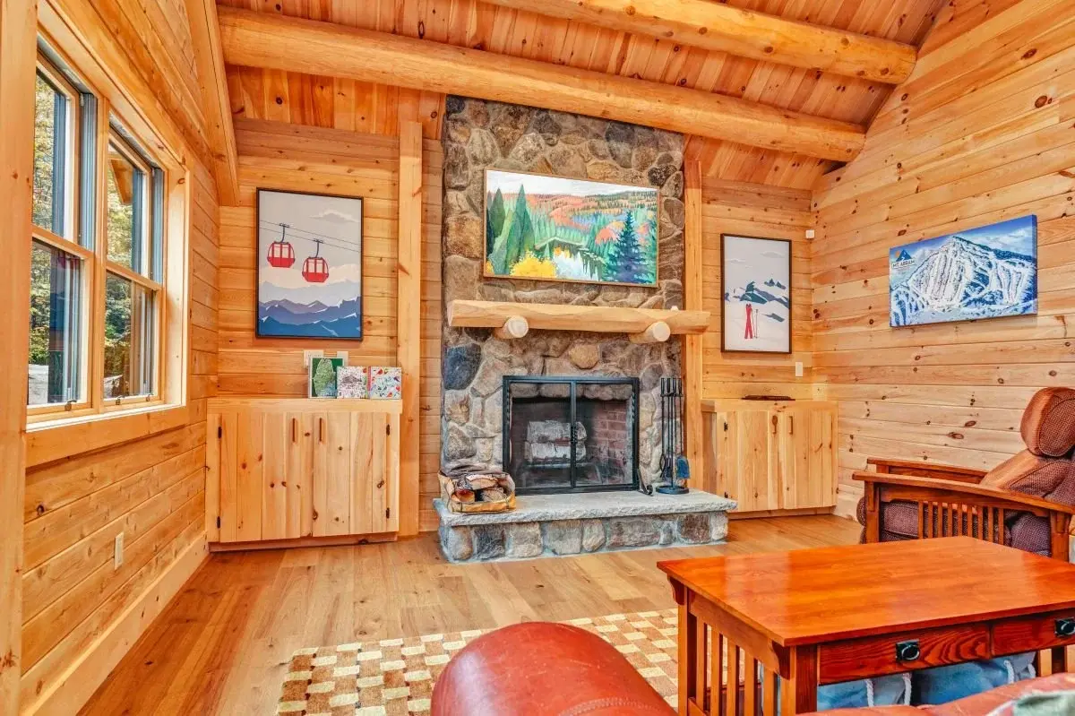 Colorful art and plenty of natural light adds to the cheerful warmth surrounding the fireplace. Practical built-in storage cabinets flank the hearth, and a chunky cedar mantle reflects the sturdy, rugged feel of the stone.