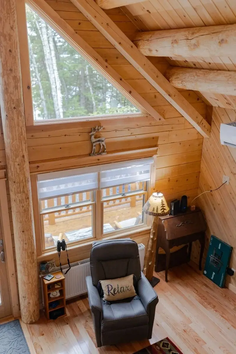 A cozy living room nook is bathed in light from windows spanning the height of the cathedral ceiling. 