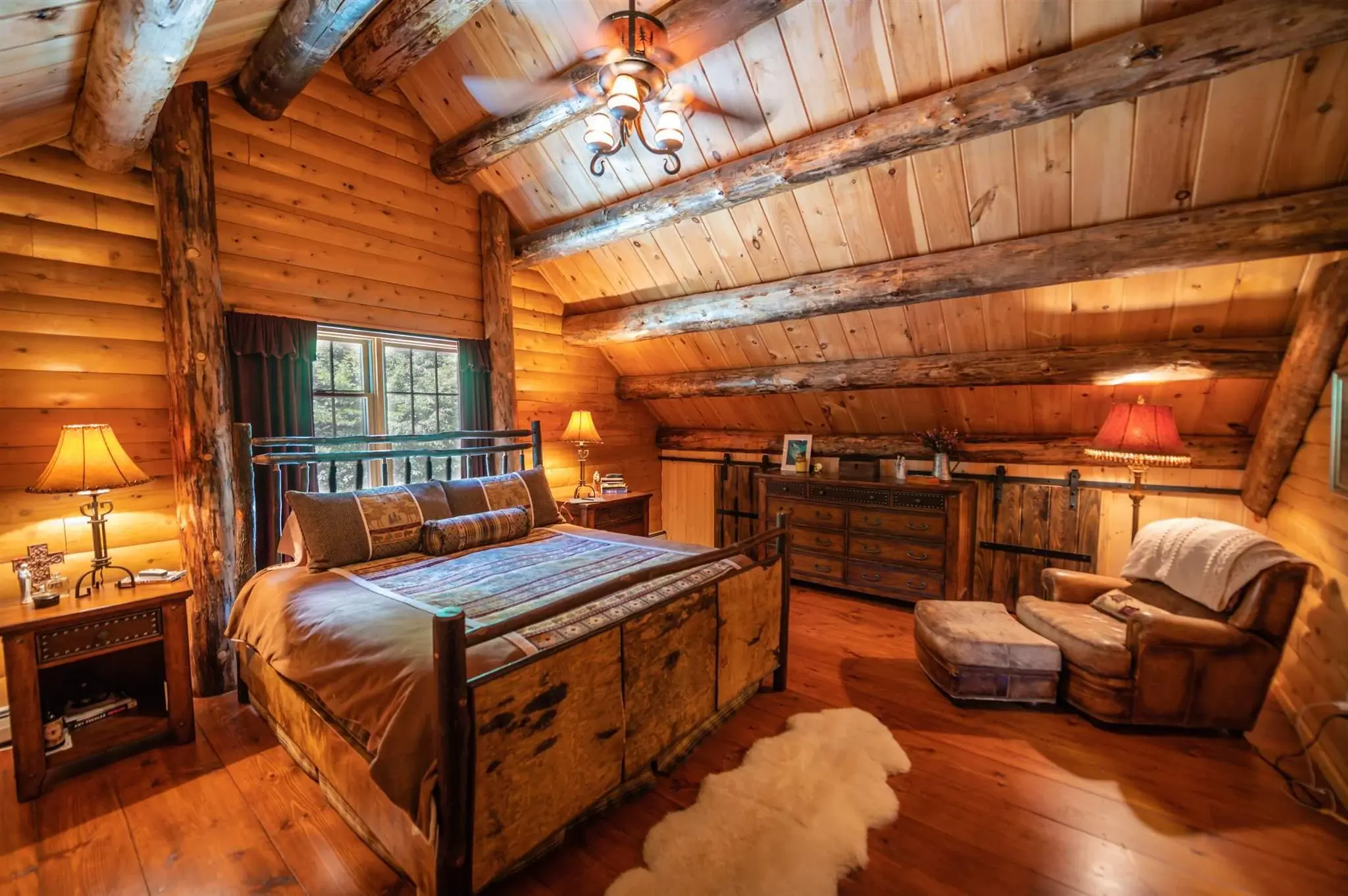 The primary bedroom echoes the grandeur of the rest of the home, with a vaulted ceiling and exposed beams. Rustic furnishings bring a timeless charm to the space. 