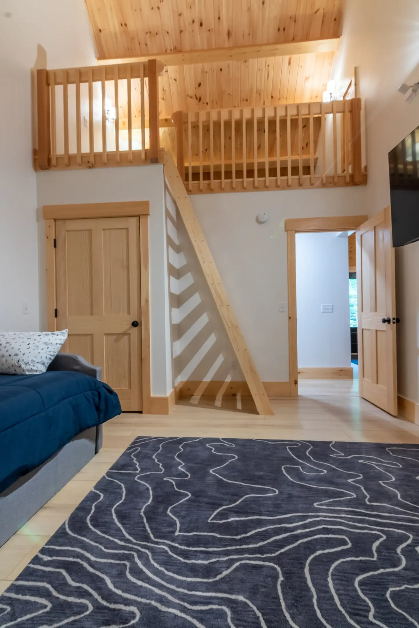 Square exposed beams on the loft ceiling give it a more modern look, tying in nicely with the abstract area rug, white walls, and simple furnishings for a room that’s contemporary and cozy. 
