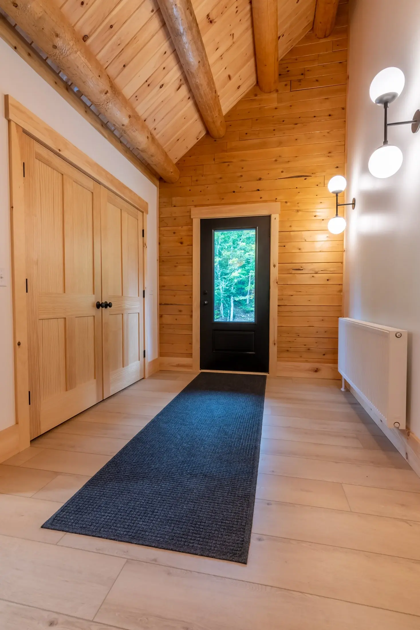 Another lesson in balancing rustic and modern is displayed here in the entry hall. The rugged ceiling beams transition easily to the warm wooden walls, while the sleek closet doors and wide paneled light flooring showcase a more refined application o
