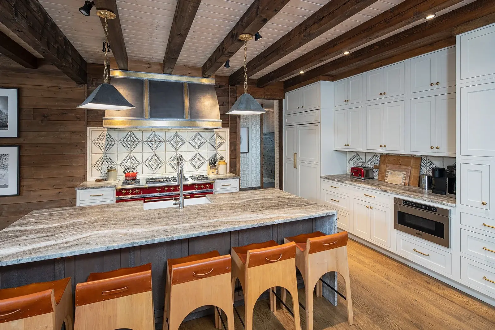 A well-organized wall of cabinets in a simple white is the perfect backdrop for the striking hearth, with its cherry red stove and sturdy, old-world hood. A tiled geometric backsplash ties it all together.   