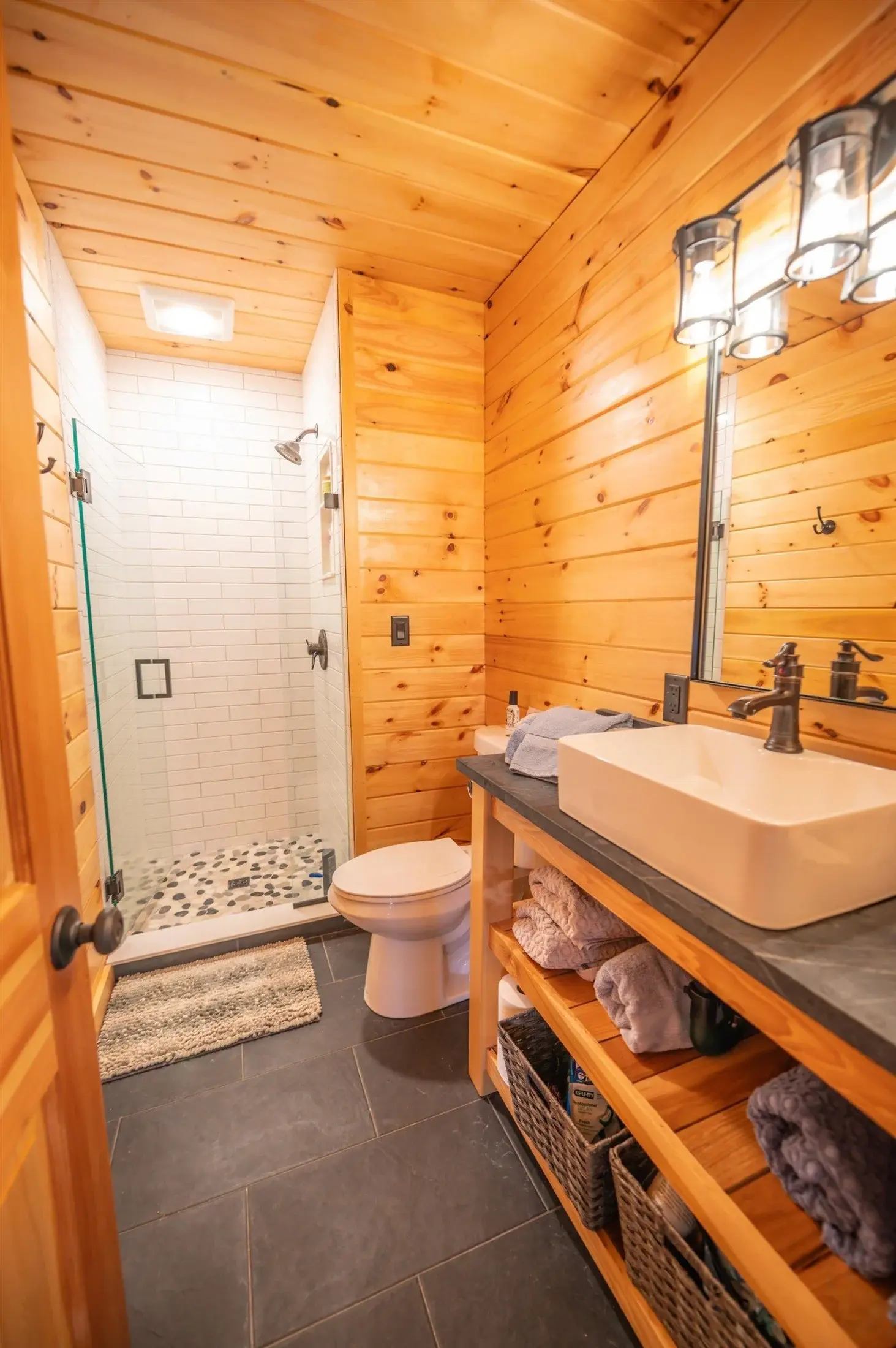 By making use of open shelving, bright white tiles, and a glass shower door, this efficiently-sized bathroom feels bright and spacious.