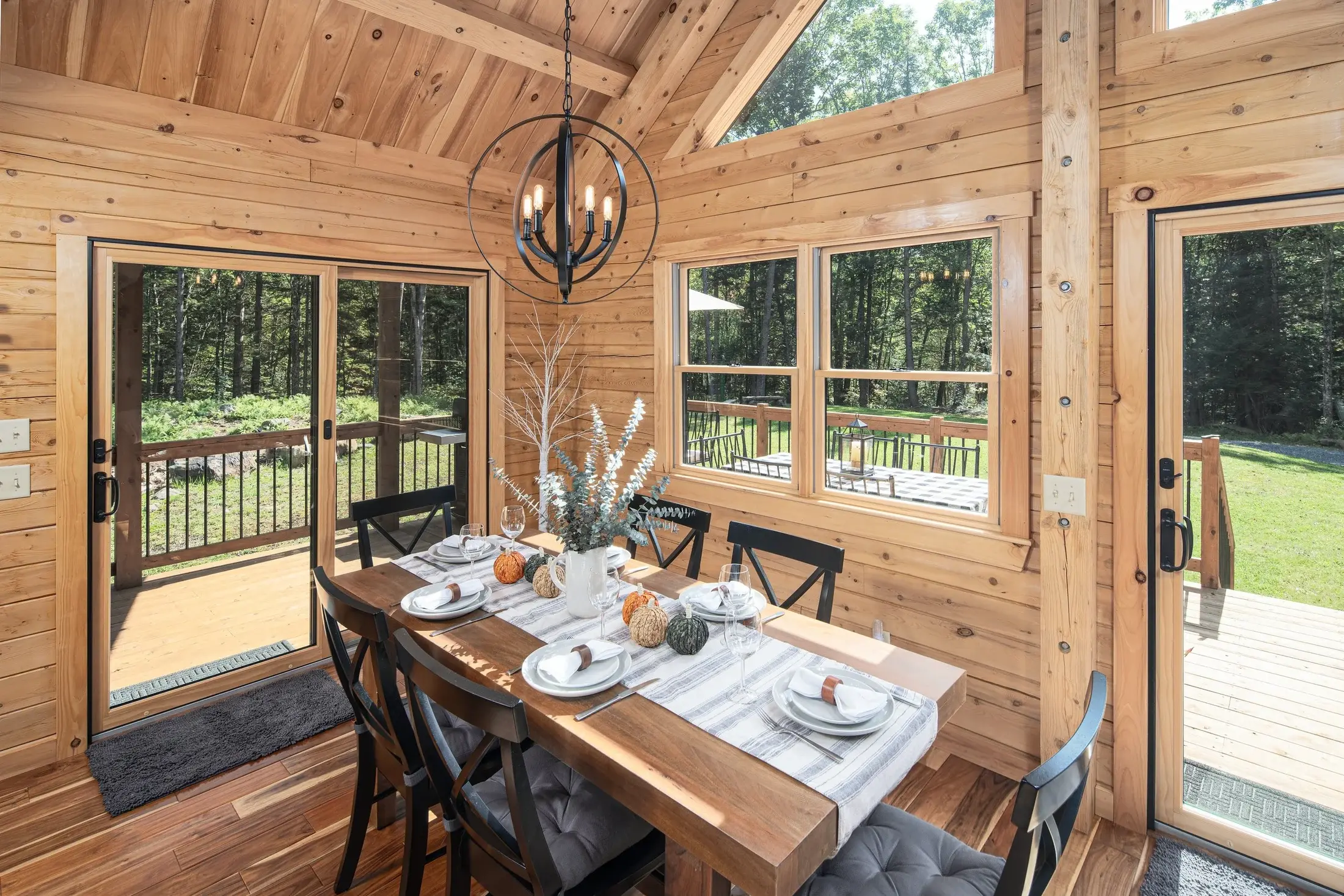 The dining room is flooded with natural light, thanks to floor to ceiling windows and two glass doors opening to the deck. The vaulted ceiling and simple chandelier add a crowning touch. 