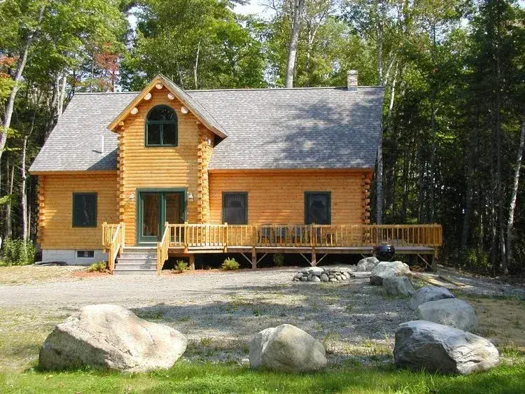 Cedar log home with a gray shingle roof, covered porch, and wooded lot from the Moosehead photo gallery